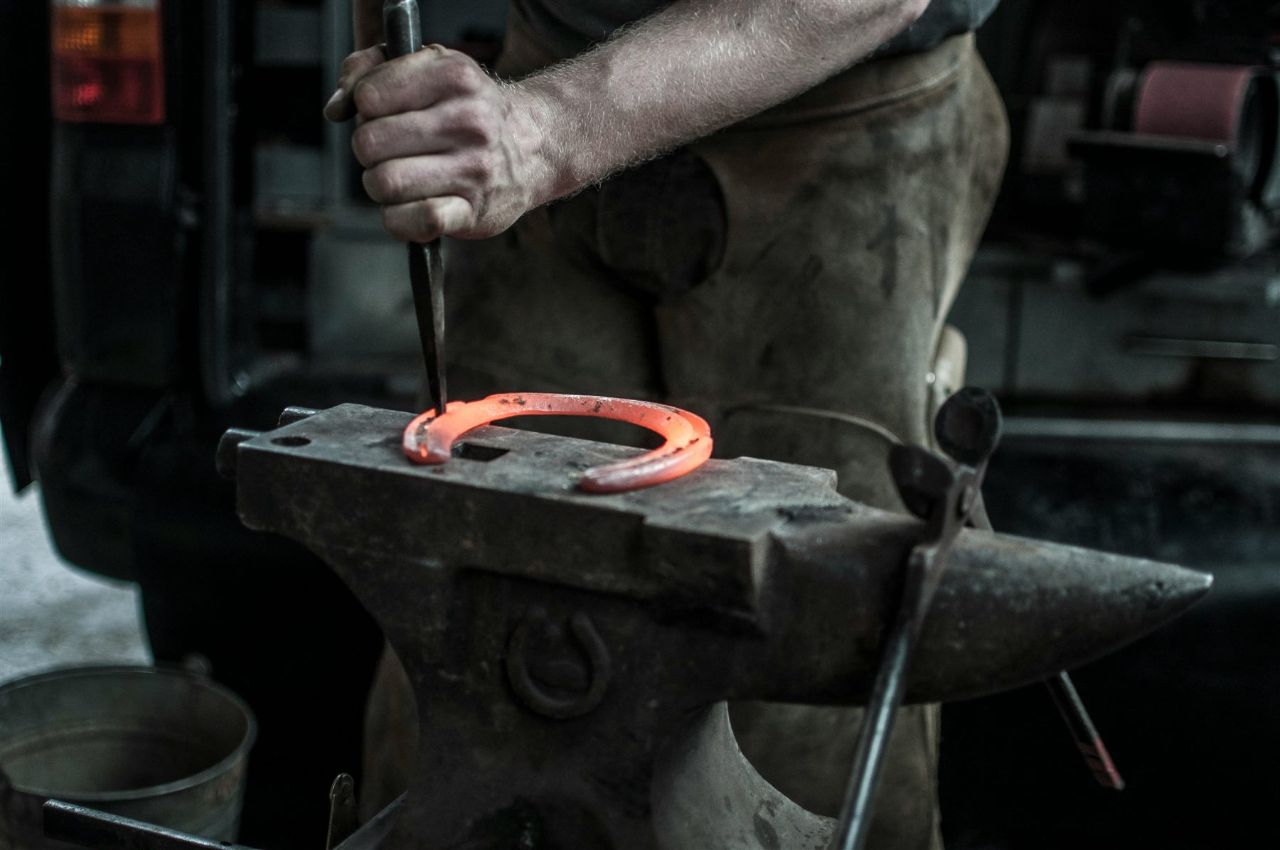 A working farrier shaping a horseshoe at the anvil
